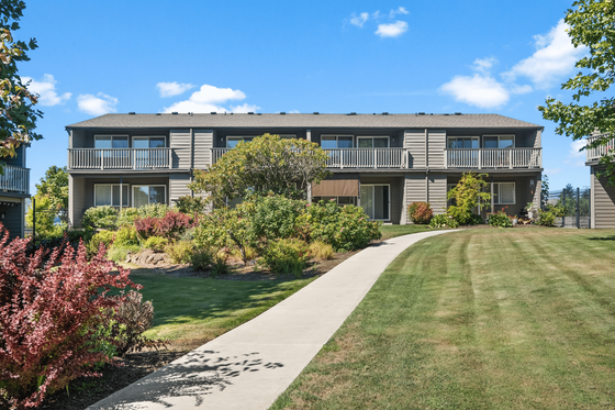 Charming apartment exterior with lush landscaping and private balconies under a bright blue sky.