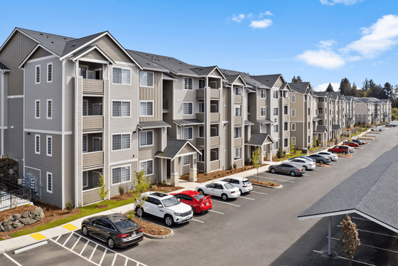 Modern apartment complex showcasing elegant multi-story buildings with private balconies and ample parking, set against a clear blue sky.