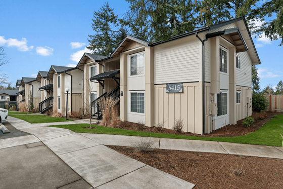 Charming apartment complex with modern architecture, featuring lush landscaping and inviting entrances under a clear blue sky.