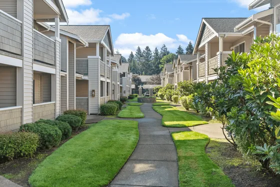 Charming apartment complex with lush green landscaping, elegant architecture, and a serene pathway.