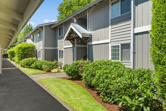Charming exterior view of an apartment complex, featuring well-maintained landscaping and modern architecture under a clear blue sky.