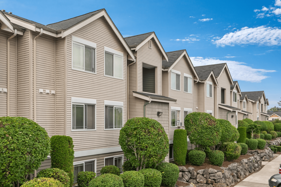 Charming townhouses with manicured landscaping, featuring modern exteriors and lush greenery under a bright blue sky.