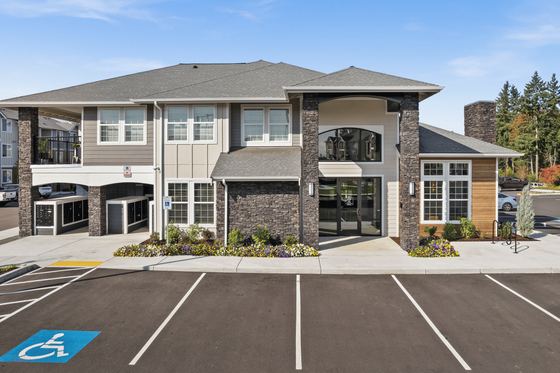 Modern apartment complex with stylish stone accents, large windows, and vibrant landscaping under a clear blue sky.