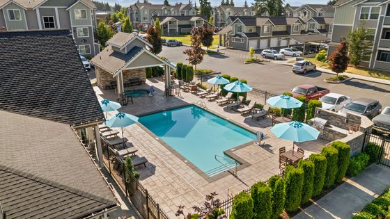 Charming apartment complex featuring a sparkling pool, inviting sun loungers, and vibrant umbrellas, surrounded by lush landscaping.