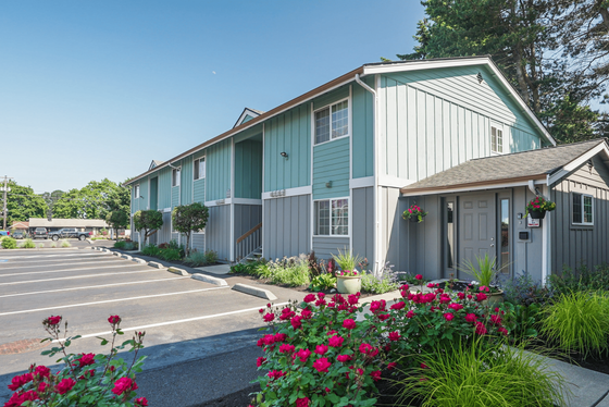 Charming two-story apartment complex with vibrant landscaping and ample parking, featuring beautiful flower beds and lush greenery.