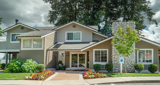 Charming suburban home with stone chimney, manicured garden, and quaint front porch under a clear sky.