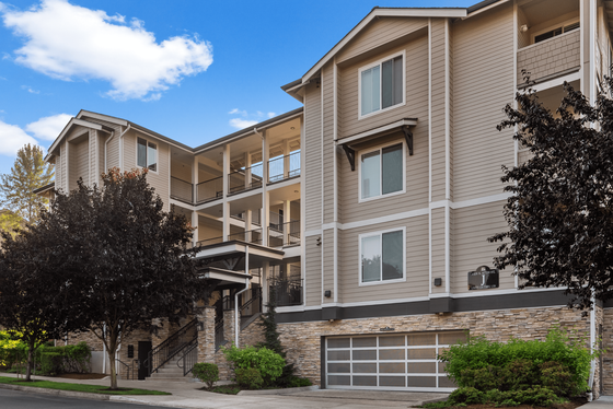 Elegant modern apartment building with spacious balconies, large windows, and lush landscaping against a vibrant blue sky.
