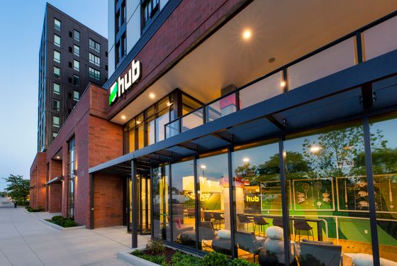 Modern urban apartment complex with sleek glass facade and warm lighting, creating an inviting atmosphere at dusk.