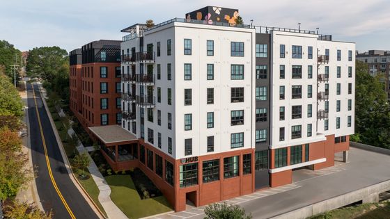 Chic modern apartment building with stylish balconies, lush green surroundings, and a vibrant rooftop mural.