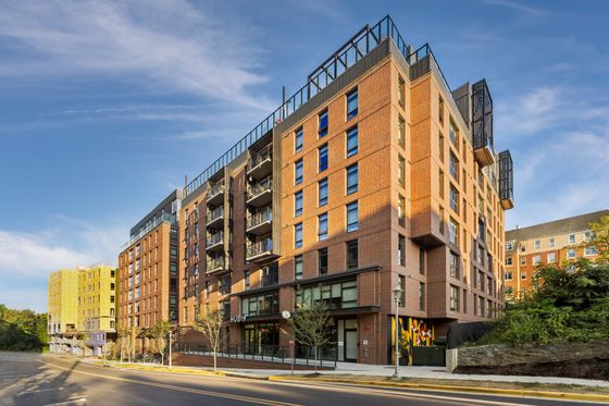 Modern apartment building with brick facade, featuring balconies and large windows, under a clear blue sky.