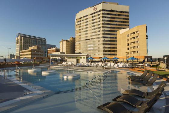 Luxurious rooftop pool with sun loungers, modern high-rise buildings in the backdrop, and vibrant cityscape views.