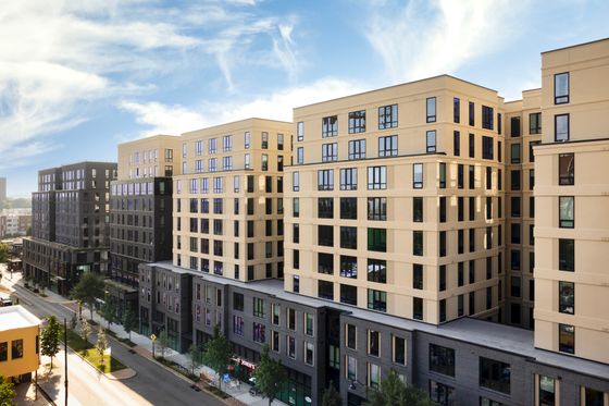 Modern urban apartment complex with contemporary architecture, featuring large windows and a vibrant street view under a clear blue sky.