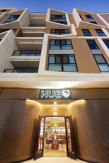 Modern apartment building facade with geometric window design and inviting 'HUB' entrance accentuated by warm lighting.