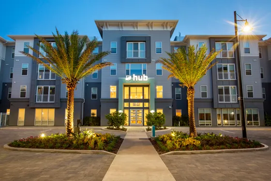Elegant apartment complex facade with modern architecture, lush landscaping, and inviting evening lighting.