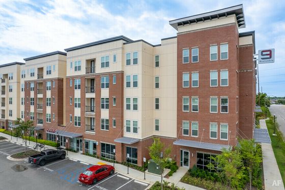 Modern apartment building featuring stylish brick and panel facade, lush landscaping, and convenient parking spaces.