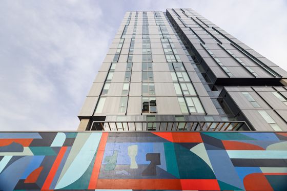 Modern high-rise apartment building with sleek glass windows, complemented by vibrant geometric street art on the facade.