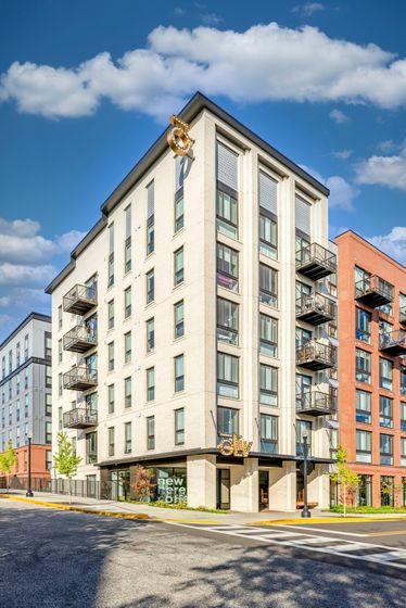 Modern multi-story apartment building with elegant balconies and vibrant street view, featuring the 'Ollie' sign against a clear blue sky.