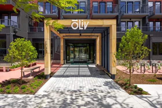 Modern apartment entrance with elegant wooden canopy and lush greenery, featuring contemporary design and inviting walkway.