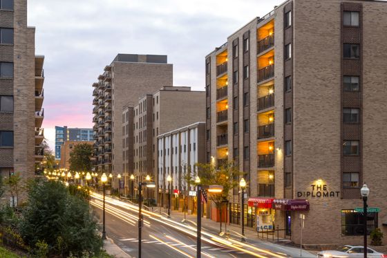 Vibrant cityscape featuring modern apartment buildings with illuminated balconies and a lively street view at dusk.