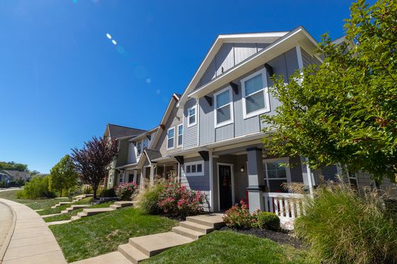 Charming suburban homes with attractive facades, colorful landscaping, and serene neighborhood sidewalk under a bright blue sky.
