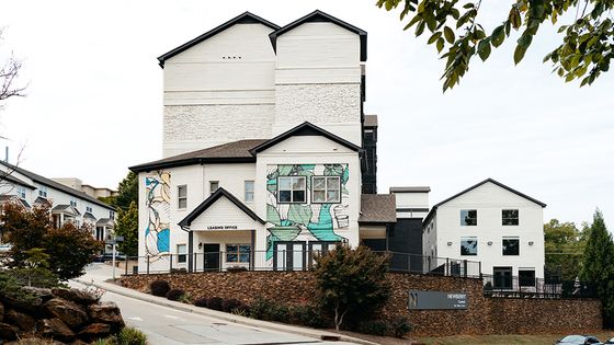 Modern apartment complex with artistic murals and welcoming leasing office, surrounded by lush greenery and stylish architecture.