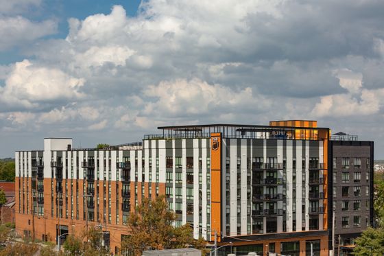 Modern urban apartment building with stylish facade and rooftop terrace under a vibrant sky.