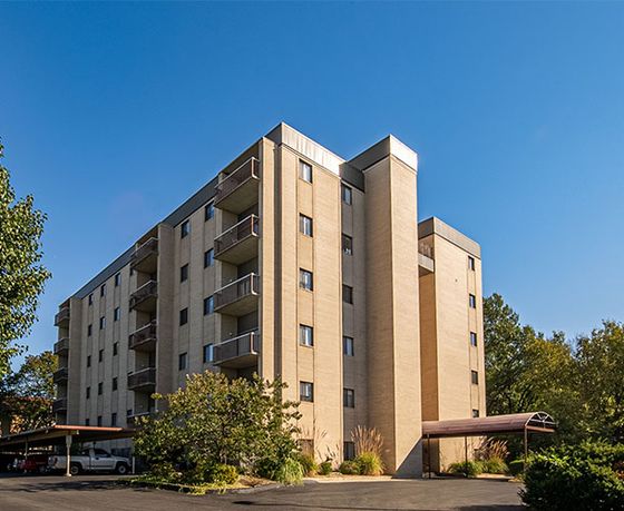 Contemporary apartment building exterior with balconies and lush greenery under a clear blue sky.
