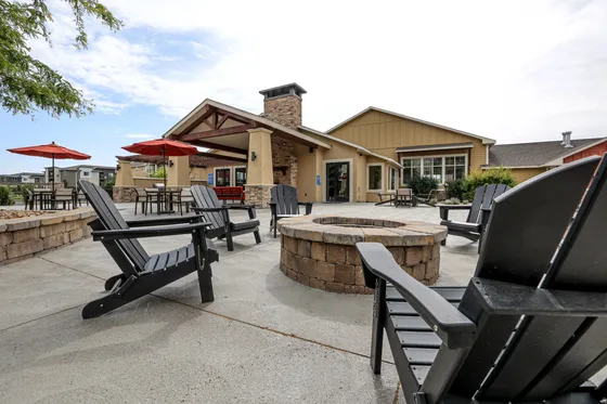 Inviting outdoor patio with cozy chairs around a fire pit, featuring red umbrellas and stone accents against a charming community building.