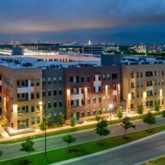 Nighttime exterior view of AMLI on Aldrich brick building exterior with lamp posts and trees lining nearby sidewalks