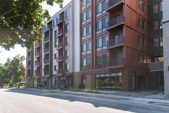Modern apartment building with sleek architecture, large windows, and private balconies set on a tree-lined street.