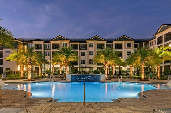 Elegant apartment building with illuminated pool and palm trees at night.