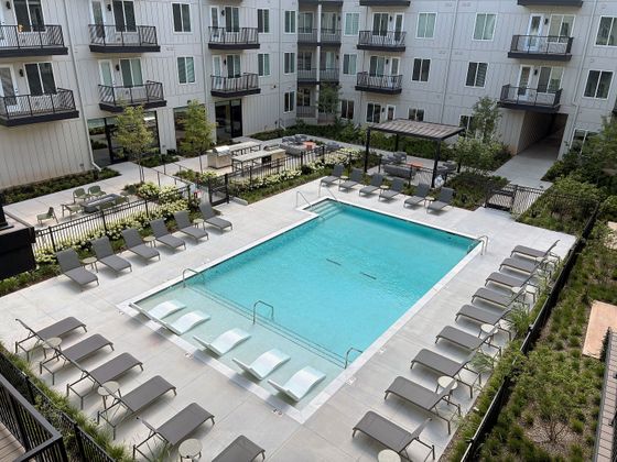 Luxurious apartment complex featuring a sparkling outdoor pool with stylish loungers, surrounded by modern balconies and lush landscaping.