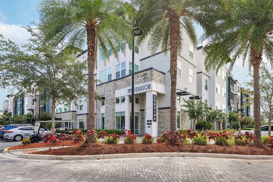 Charming exterior of The Addison with palm trees, stone accents, and a welcoming entrance, exuding modern elegance.