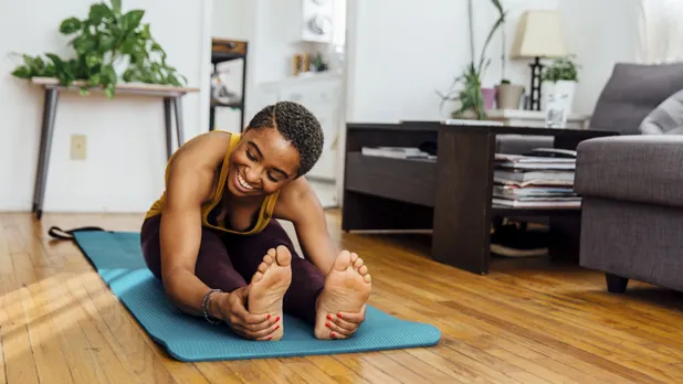 woman stretching on yoga mat in living room of apartment