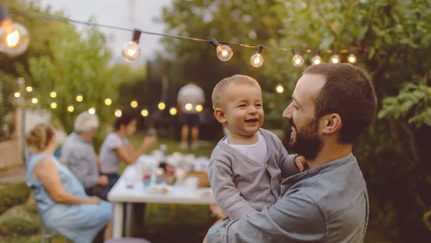 man with baby in arms in outdoor barbecue in daytime with stringlights on