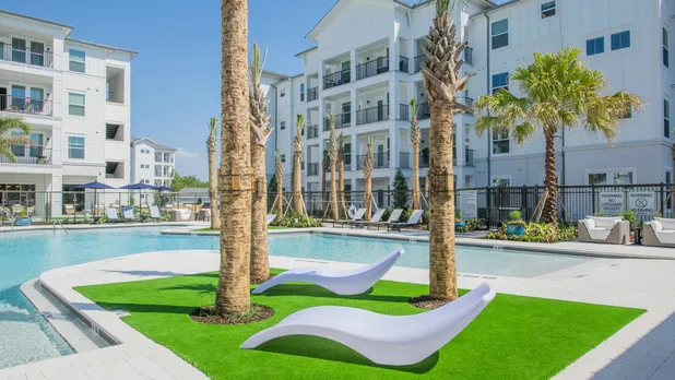 exterior pool with lounge chairs and apartment building behind it in daytime