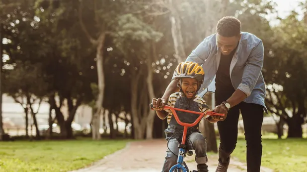 man helping young boy ride bicycle in park outdoors on sunny day