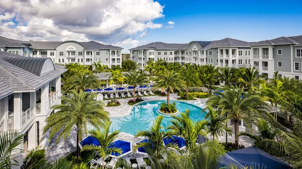 View of exterior of community with pool and palm trees in the daytime