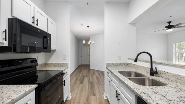 Galley kitchen with white cabinets, wood style flooring and black appliances