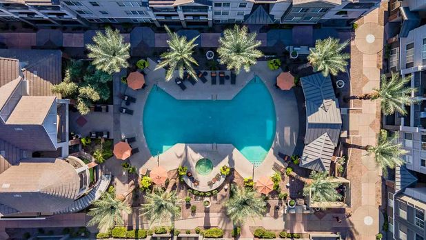 Aerial view of a luxurious apartment complex featuring a spacious swimming pool surrounded by palm trees and lounge areas.