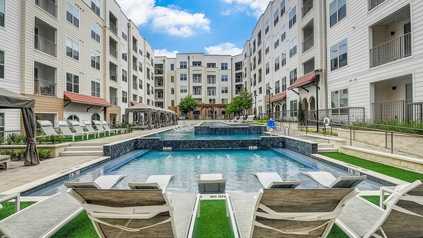Modern apartment complex with a luxurious outdoor pool and sun loungers under a blue sky.