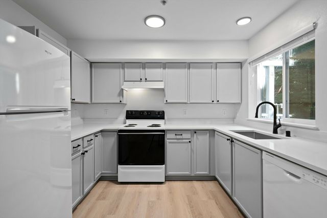 Modern kitchen with sleek white cabinetry, stainless steel appliances, and large window offering natural light.