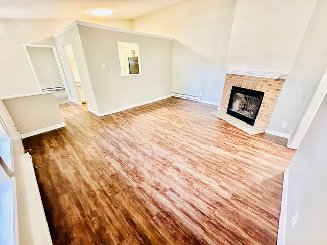 Bright open living room with wood flooring and a cozy brick fireplace.