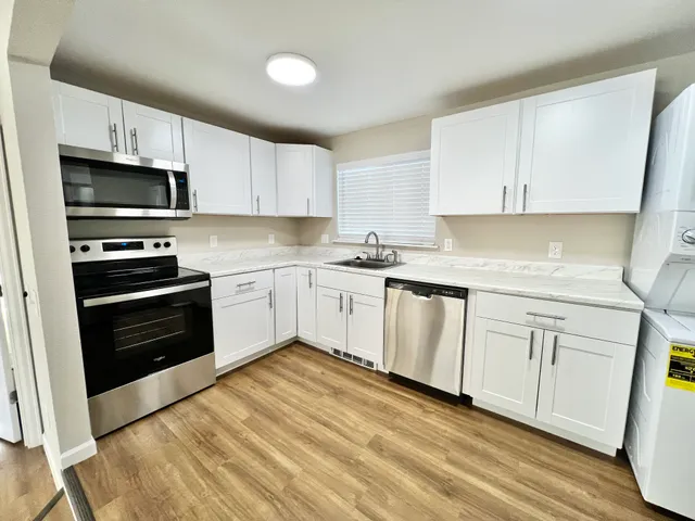 Bright kitchen with sleek white cabinets, stainless steel appliances, and wooden flooring.