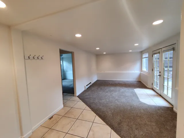 Bright living room with tile and carpet flooring, featuring French doors and recessed lighting.