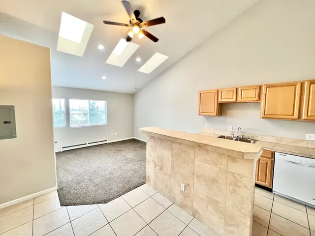 Spacious living area with vaulted ceilings, skylights, and adjacent kitchen featuring wooden cabinets and a breakfast bar.