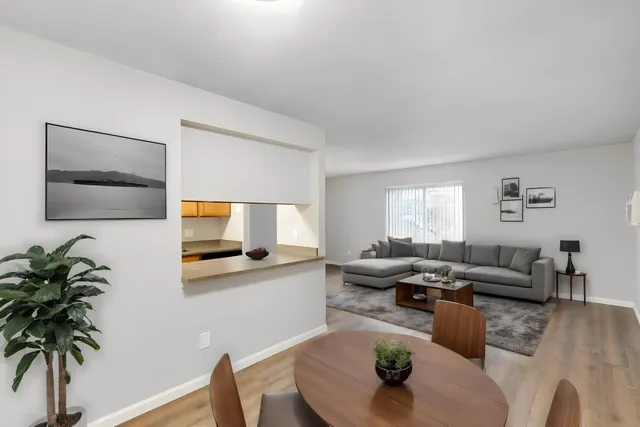 Stylish open-plan living room with modern gray sofa, dining area, and kitchen view.