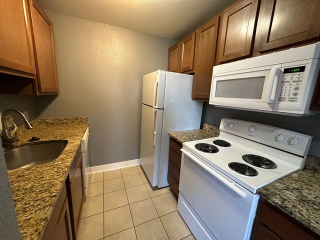 Compact kitchen with granite countertops, white appliances, and wood cabinetry.