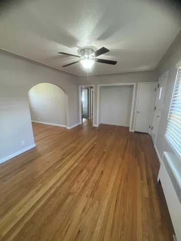 Bright living area with polished hardwood floors and a ceiling fan, featuring an arched doorway.