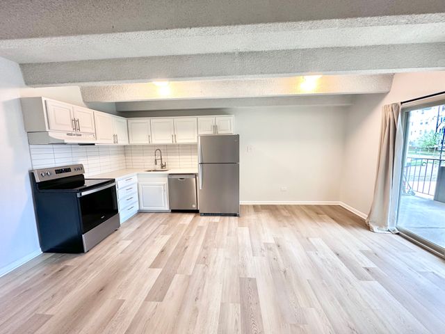 Bright modern kitchen with stainless appliances, sleek white cabinets, and open layout leading to a balcony.